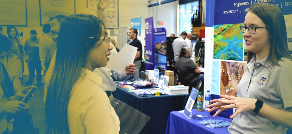 A recruiter standing in front of a booth talks to a student at a job fair at a Western New York Works college
