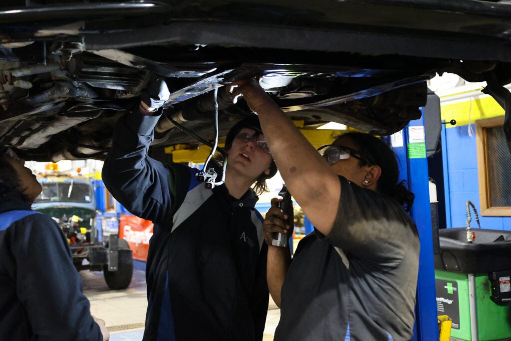 A student and instructor examine the undercarriage of a lifted car in an auto repair class at Alfred State College