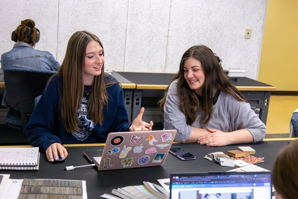 Interior Design students in a class at Alfred State College converse around a table featuring several color and pattern samples