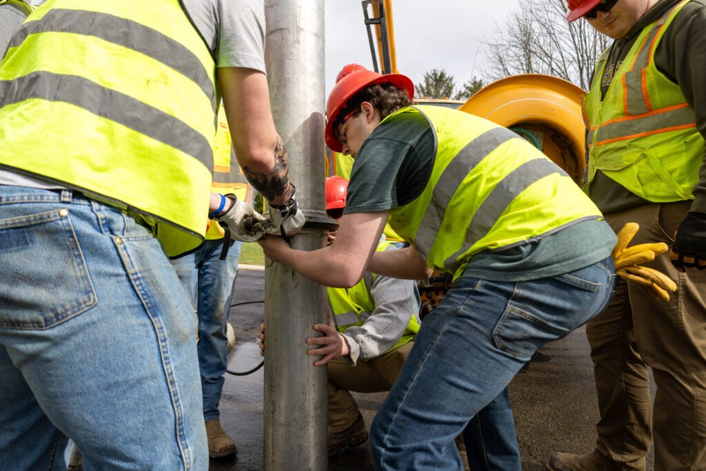 Wearing ANSI safety vests, students in a heavy equipment class at Alfred State College learn to clean sewer pipes
