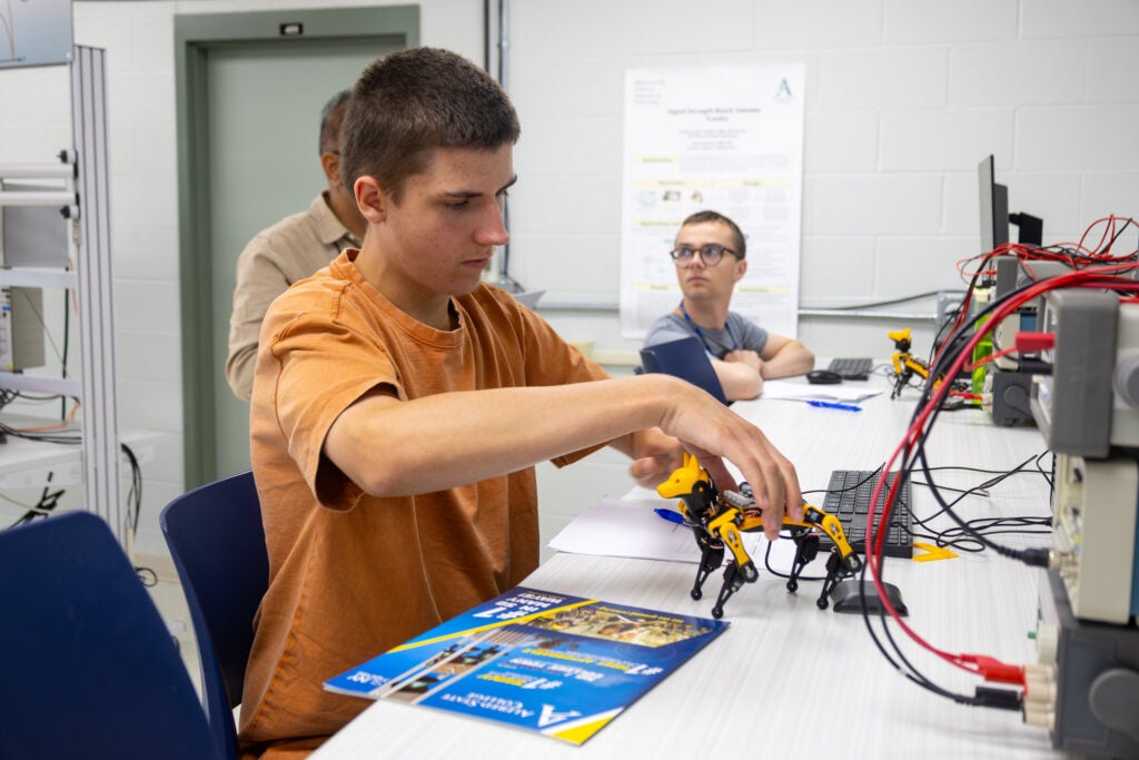 A student positions a small robotic dog on a table in a robotics class open to high schoolers at Alfred State College